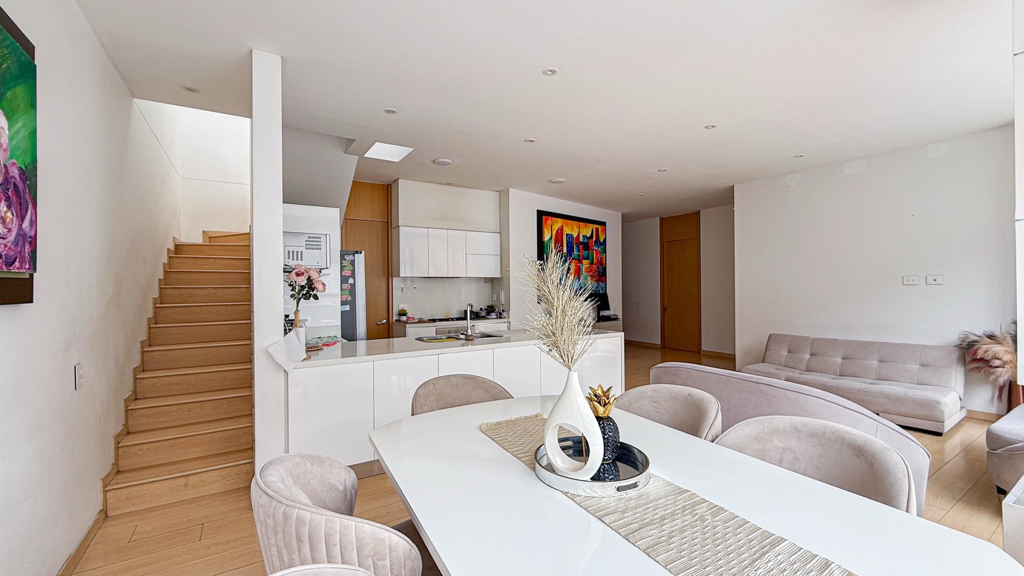 Zona social del penthouse con comedor, cocina abierta y escalera a la terraza
